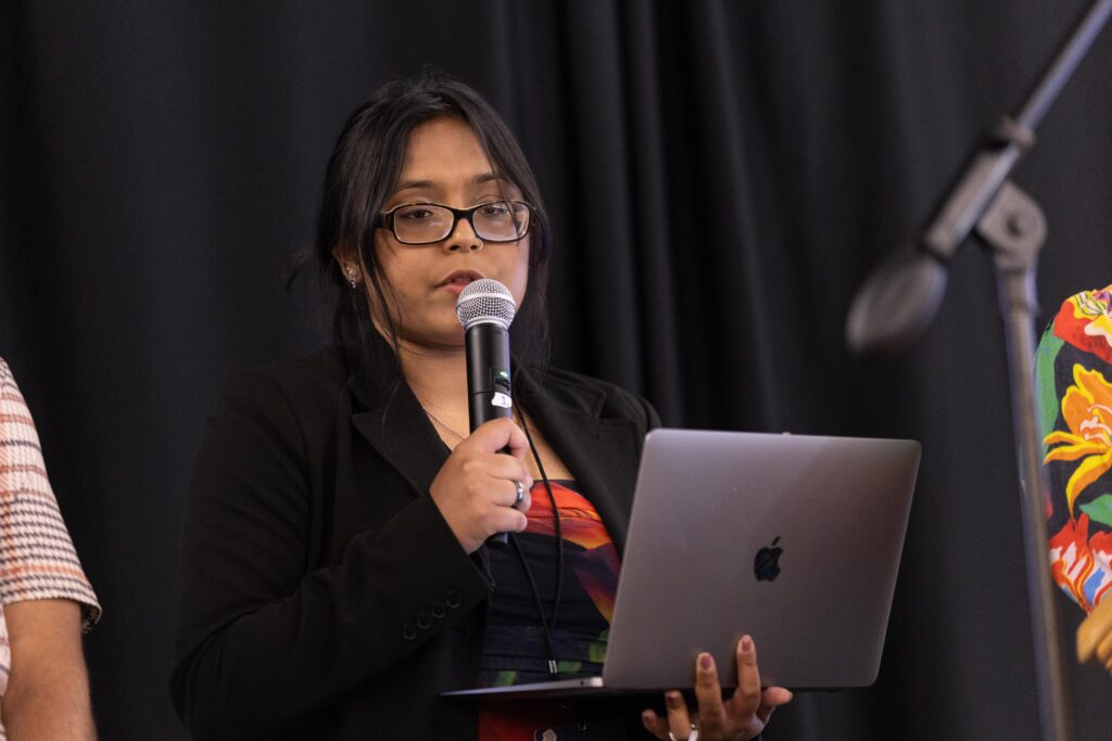 Naeema holds her laptop and the microphone as she talks about Mapping for Equity.