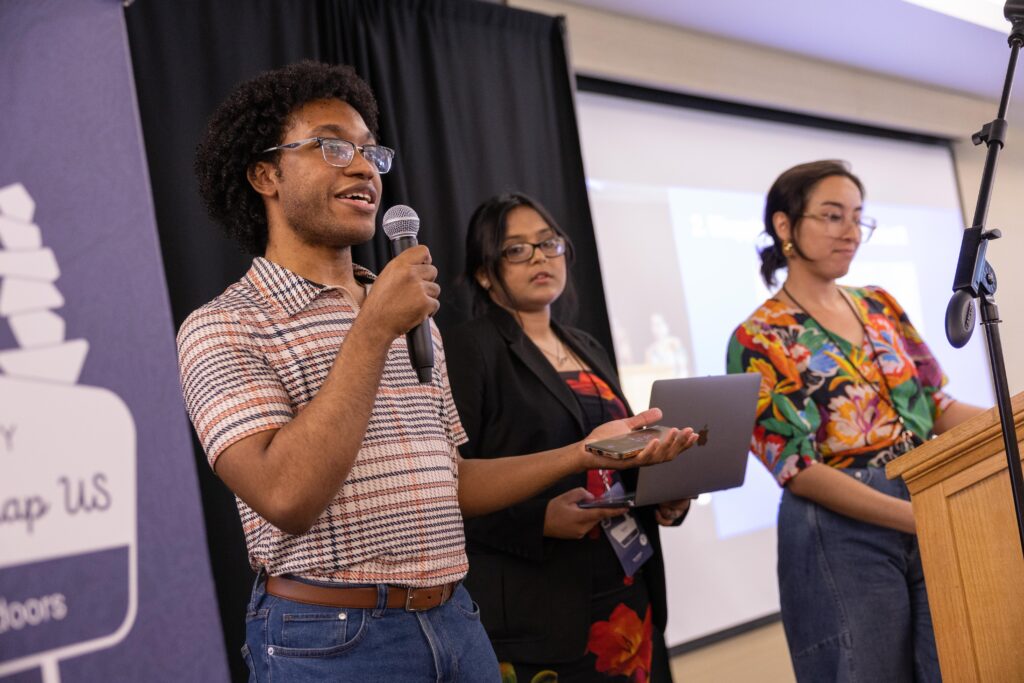 Dimitri speaks into the microphone as he presents on Mapping for Equity. 