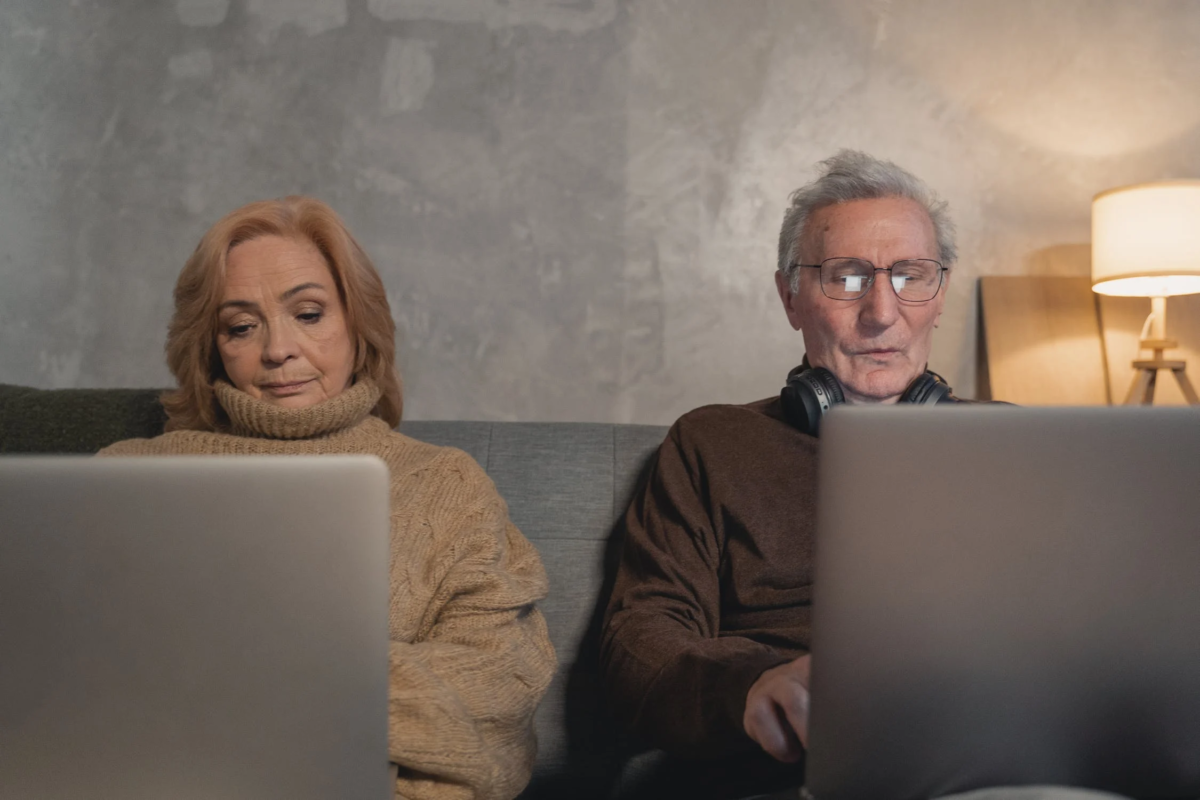 Eldery man and women sitting on couch using laptop