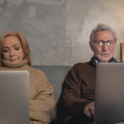 Eldery man and women sitting on couch using laptop